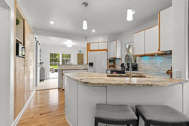kitchen with light wood finished floors, decorative backsplash, white refrigerator with ice dispenser, and a peninsula