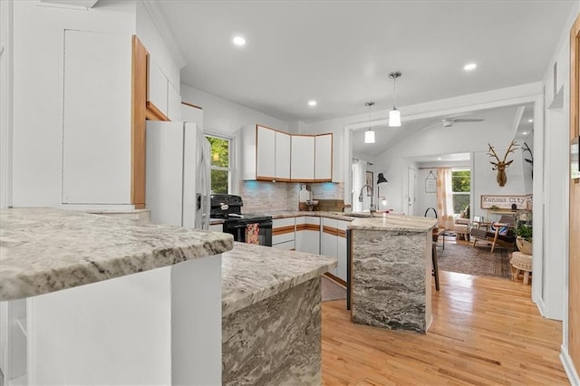 kitchen featuring black range with electric cooktop, a peninsula, light wood-type flooring, tasteful backsplash, and a sink