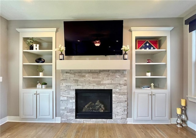 unfurnished living room featuring a stone fireplace, baseboards, built in features, and wood finished floors