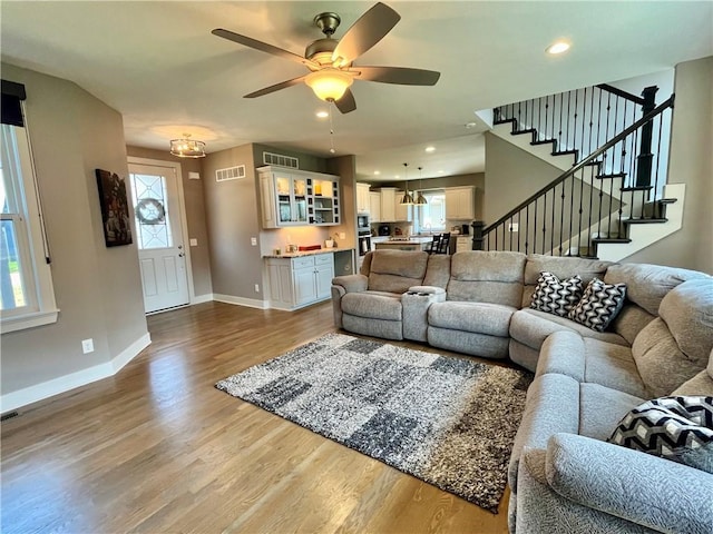 living area with ceiling fan, baseboards, wood finished floors, visible vents, and stairway