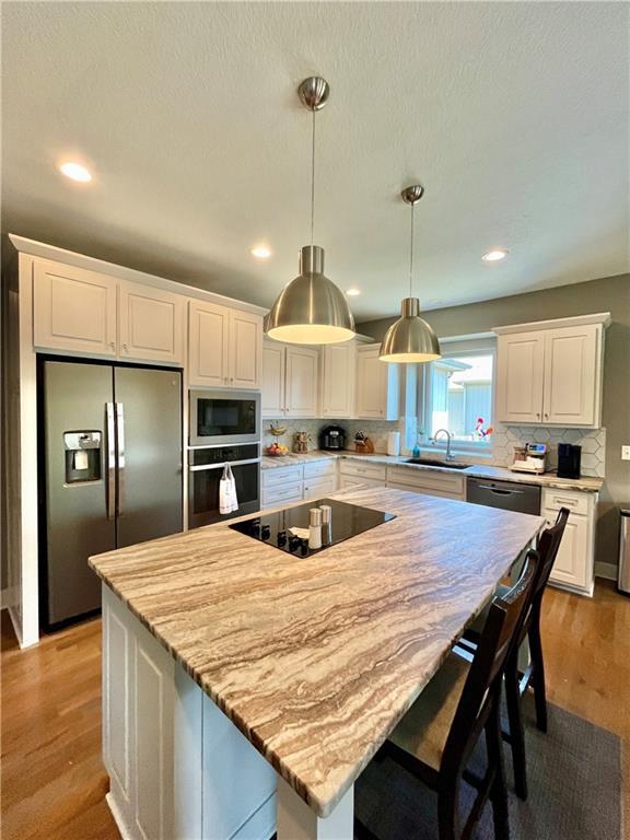 kitchen with a sink, white cabinets, black appliances, and light wood-style flooring