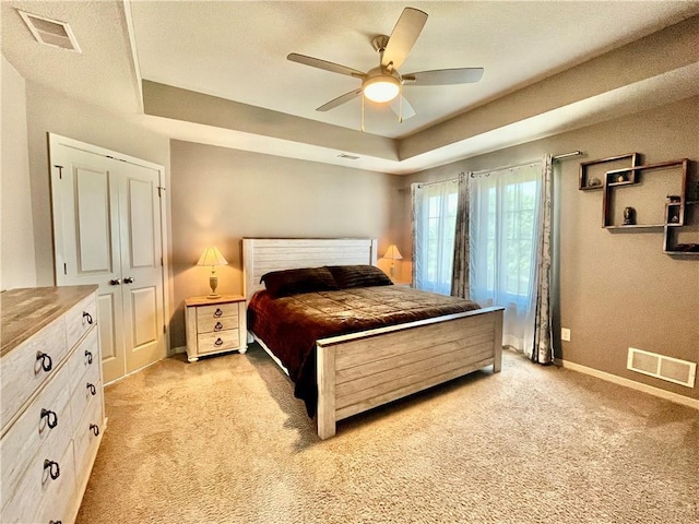 bedroom featuring a tray ceiling, visible vents, and light carpet