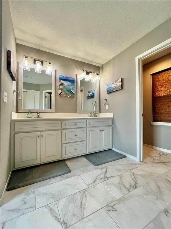 full bath with baseboards, double vanity, marble finish floor, and a textured ceiling