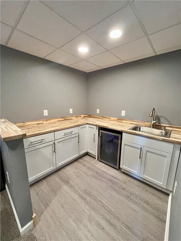 bar with a paneled ceiling, light wood-type flooring, a sink, indoor wet bar, and wine cooler