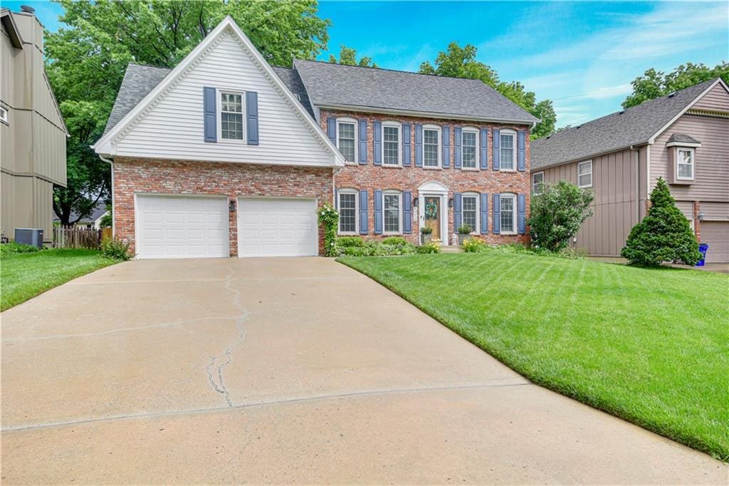 14406 W 84th Ter, Lenexa, KS 66215 - colonial house featuring brick siding, central AC unit, a garage, concrete driveway, and a front lawn