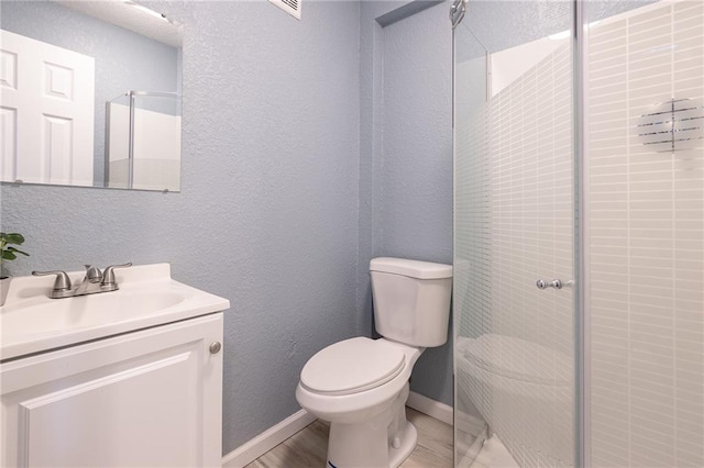 full bathroom featuring a stall shower, vanity, baseboards, toilet, and a textured wall