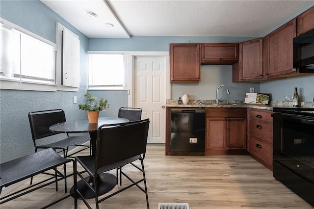 kitchen featuring light stone countertops, a textured wall, a sink, light wood-style floors, and black appliances