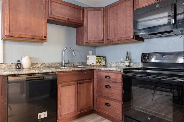 kitchen featuring light stone counters, a sink, brown cabinets, and black appliances