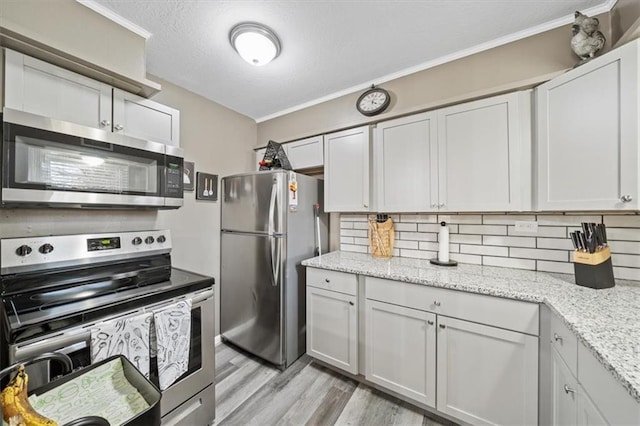 kitchen featuring backsplash, light stone countertops, ornamental molding, stainless steel appliances, and light wood-style flooring