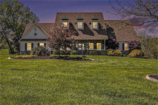 cape cod house with a front yard, a shingled roof, and stone siding