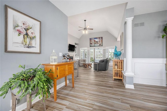 interior space featuring visible vents, decorative columns, high vaulted ceiling, a wainscoted wall, and light wood finished floors