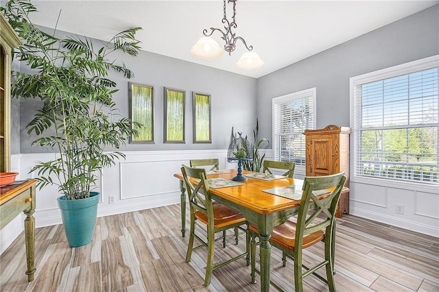 dining room featuring a healthy amount of sunlight, an inviting chandelier, a decorative wall, and light wood-type flooring