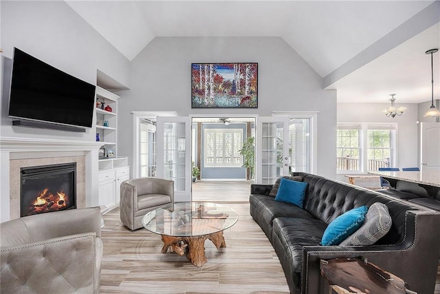 living room with an inviting chandelier, a fireplace, high vaulted ceiling, french doors, and light wood finished floors