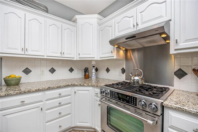 kitchen featuring under cabinet range hood, white cabinetry, stainless steel gas range oven, and tasteful backsplash