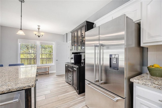 kitchen featuring light stone countertops, light wood-style floors, a notable chandelier, decorative light fixtures, and stainless steel appliances