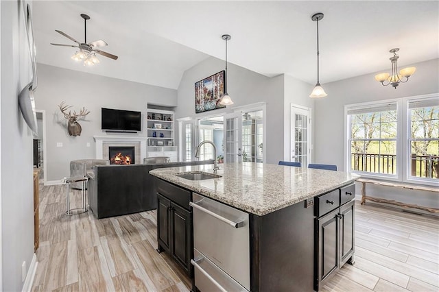 kitchen featuring a sink, ceiling fan with notable chandelier, open floor plan, stainless steel dishwasher, and a lit fireplace