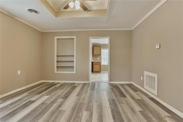 spare room featuring built in shelves, light wood-type flooring, a ceiling fan, ornamental molding, and baseboards