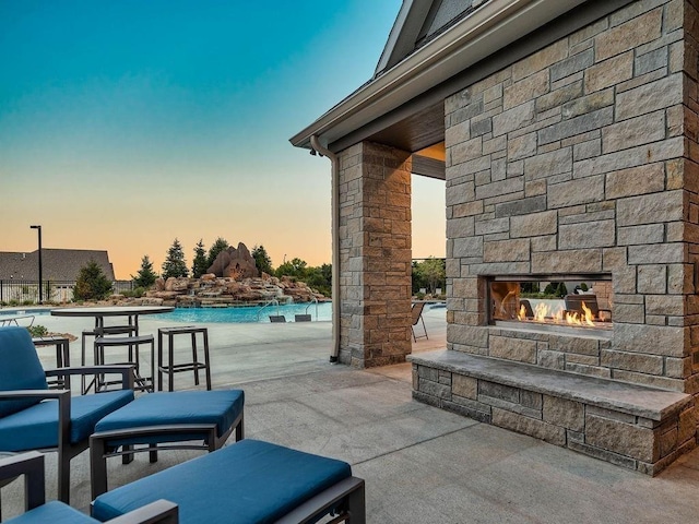patio terrace at dusk featuring a community pool and an outdoor stone fireplace