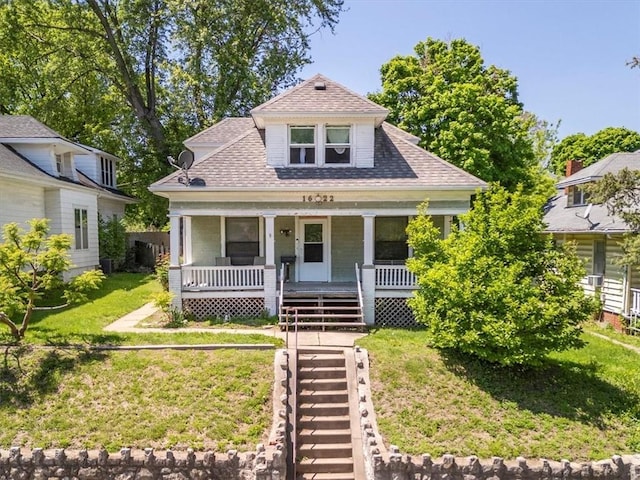 bungalow-style home with roof with shingles, a front yard, and covered porch