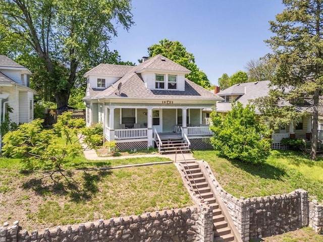 view of front of property with covered porch, a front lawn, and a shingled roof