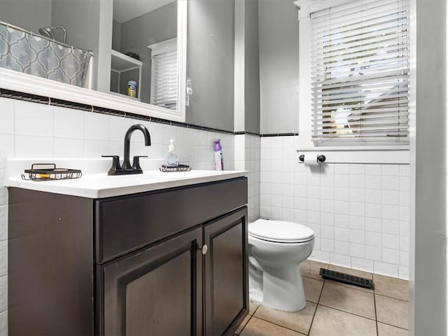 bathroom with tile walls, toilet, tile patterned floors, vanity, and curtained shower