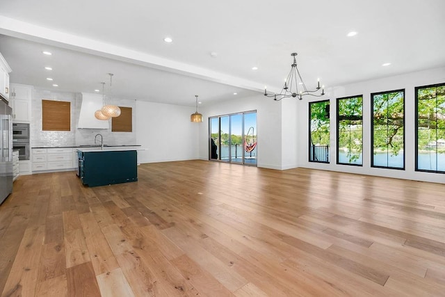 unfurnished living room with an inviting chandelier, a sink, recessed lighting, light wood-type flooring, and beamed ceiling