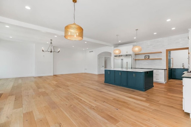 kitchen featuring arched walkways, open shelves, light wood-style floors, stainless steel built in refrigerator, and white cabinetry