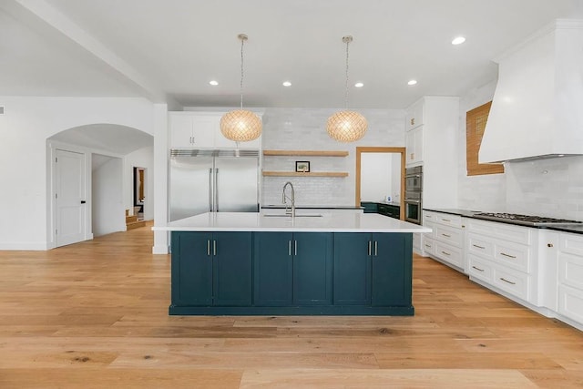 kitchen featuring open shelves, appliances with stainless steel finishes, a sink, arched walkways, and tasteful backsplash