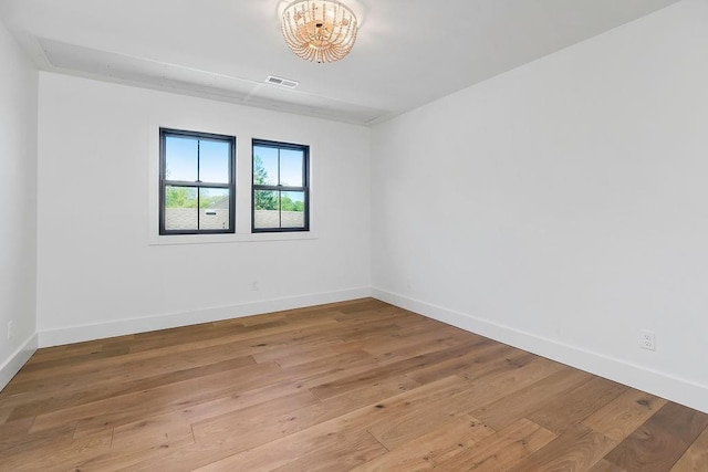 spare room featuring wood-type flooring, a chandelier, baseboards, and visible vents