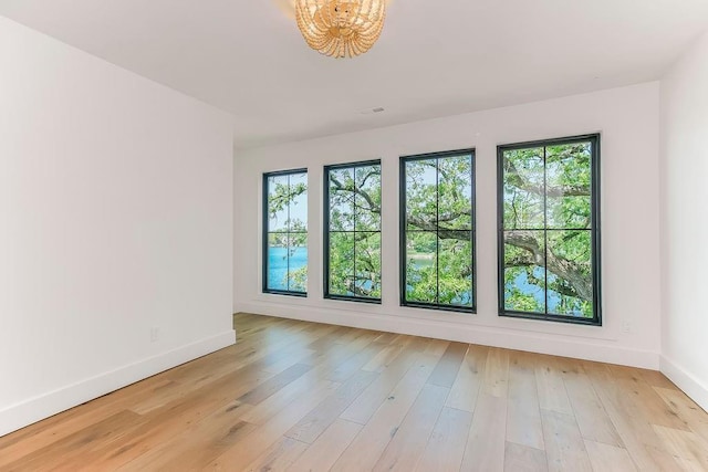 unfurnished room featuring plenty of natural light, baseboards, light wood finished floors, and an inviting chandelier