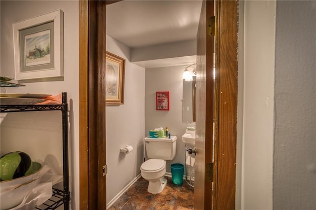 bathroom with baseboards, stone finish flooring, and toilet