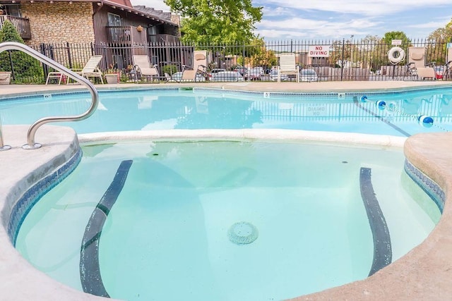 view of swimming pool with fence and a pool with connected hot tub