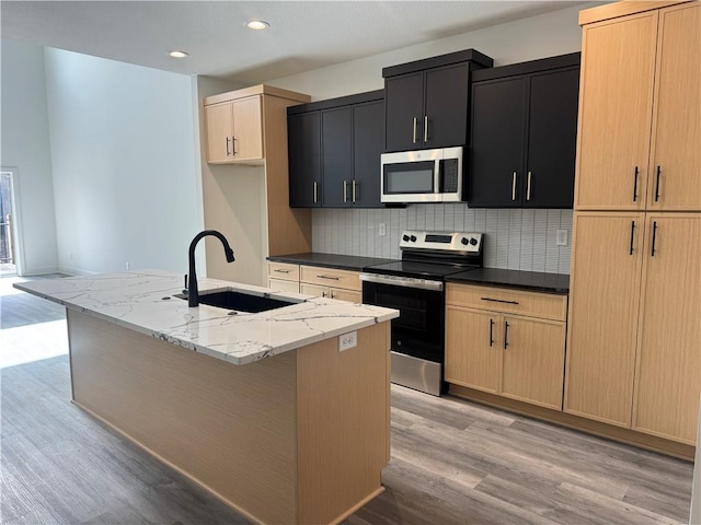 kitchen featuring a sink, appliances with stainless steel finishes, light wood-type flooring, and an island with sink