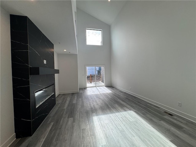 unfurnished living room featuring a fireplace, wood finished floors, a wealth of natural light, and high vaulted ceiling