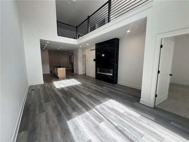 unfurnished living room featuring baseboards, a sink, a towering ceiling, and wood finished floors