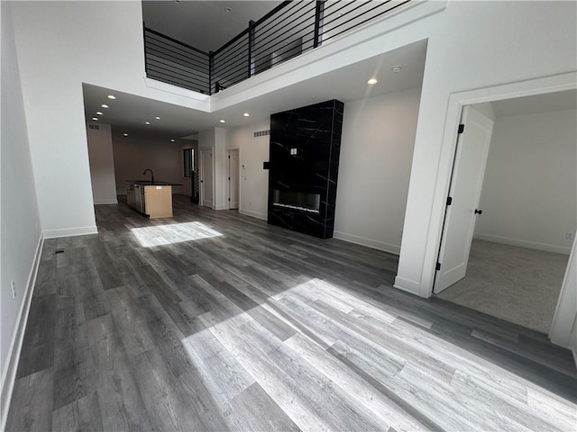 unfurnished living room featuring baseboards, a sink, a towering ceiling, and wood finished floors
