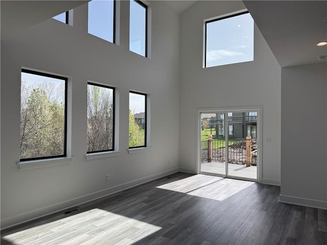 empty room featuring baseboards, wood finished floors, and a towering ceiling