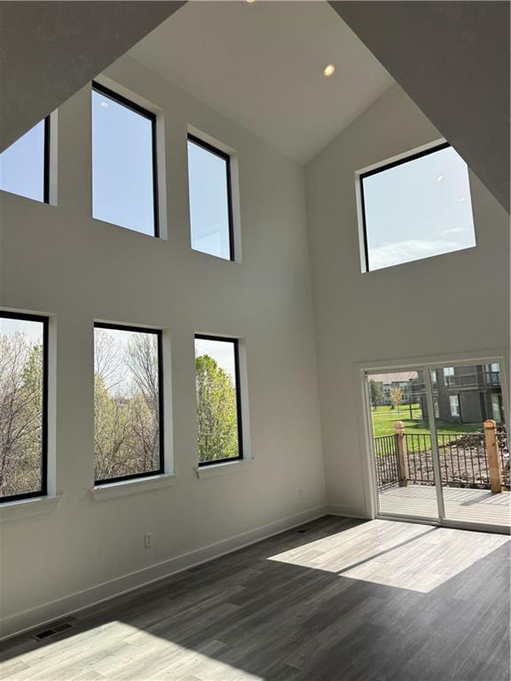 empty room with baseboards, recessed lighting, wood finished floors, and high vaulted ceiling