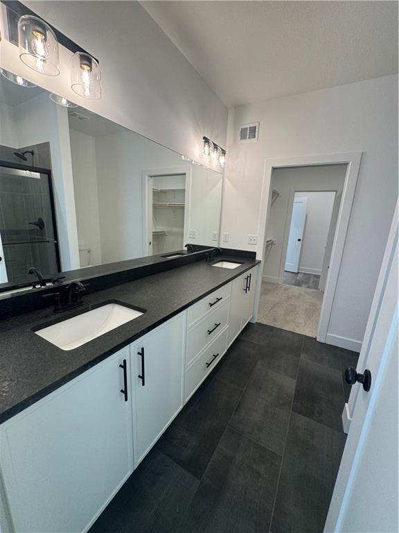 bathroom with double vanity, visible vents, a shower stall, and a sink