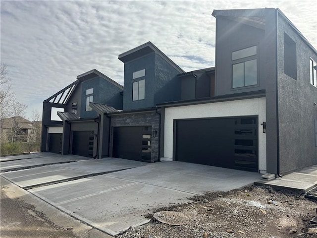 contemporary house featuring stone siding, stucco siding, a standing seam roof, an attached garage, and driveway