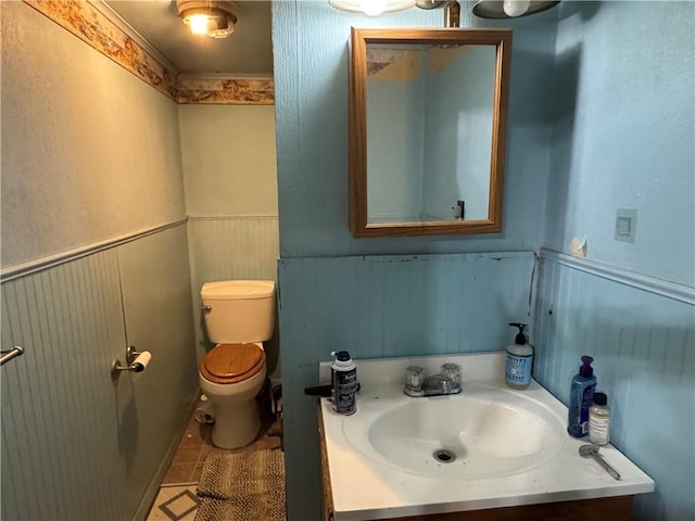 half bath featuring vanity, toilet, and a wainscoted wall