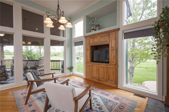 living area featuring crown molding, a high ceiling, a notable chandelier, and visible vents