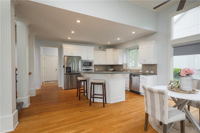 kitchen featuring a kitchen island, a kitchen bar, white cabinetry, stainless steel appliances, and light wood-style flooring