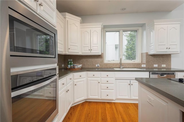 kitchen with dark countertops, tasteful backsplash, a sink, white cabinets, and stainless steel appliances