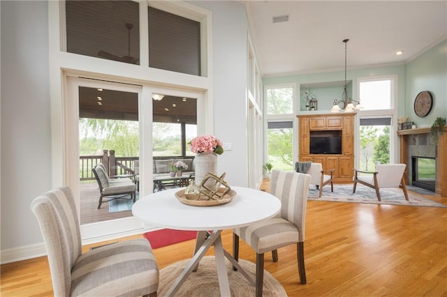 dining room with crown molding, visible vents, baseboards, a tile fireplace, and light wood finished floors