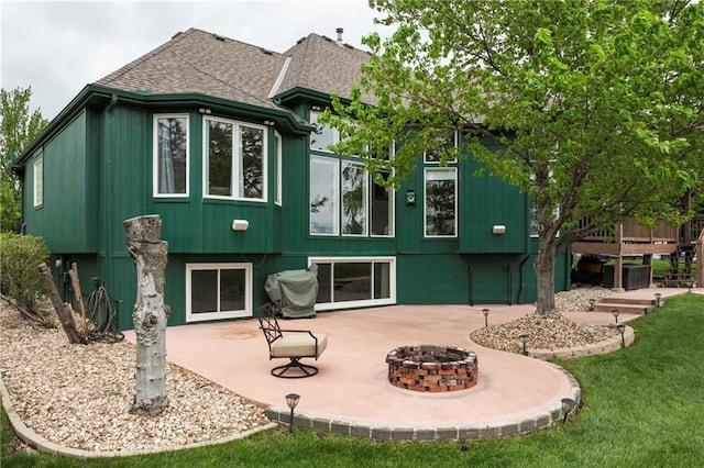 rear view of property with a wooden deck, a shingled roof, a patio area, a lawn, and an outdoor fire pit