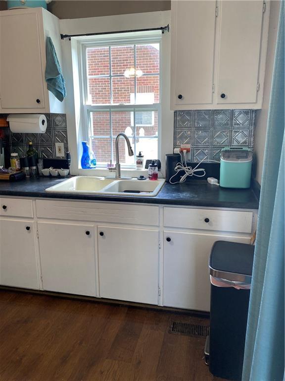 1404 S Barrett Ave, Sedalia, MO 65301 - kitchen with decorative backsplash, dark wood-style flooring, dark countertops, white cabinets, and a sink