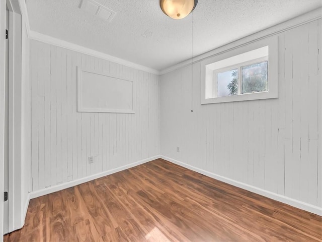 empty room featuring a textured ceiling, visible vents, crown molding, wood finished floors, and baseboards