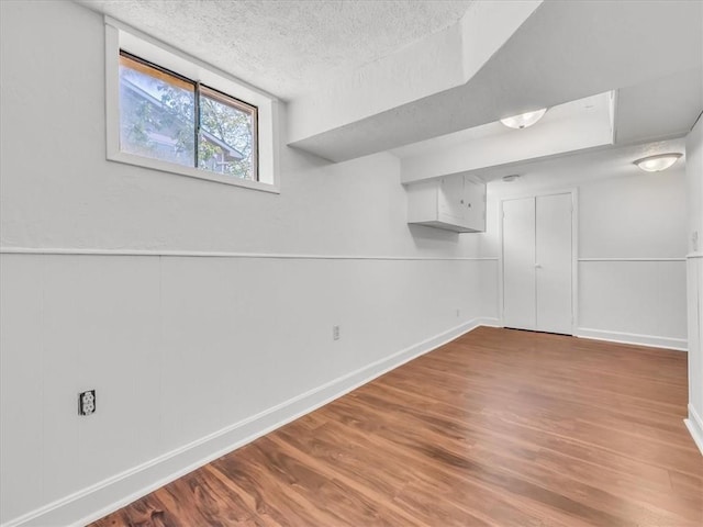 below grade area with a textured ceiling, baseboards, and wood finished floors