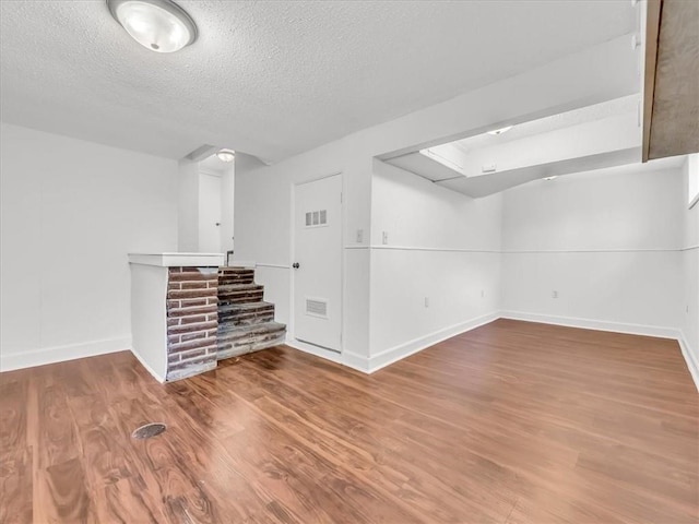 finished basement featuring a textured ceiling, visible vents, baseboards, and wood finished floors